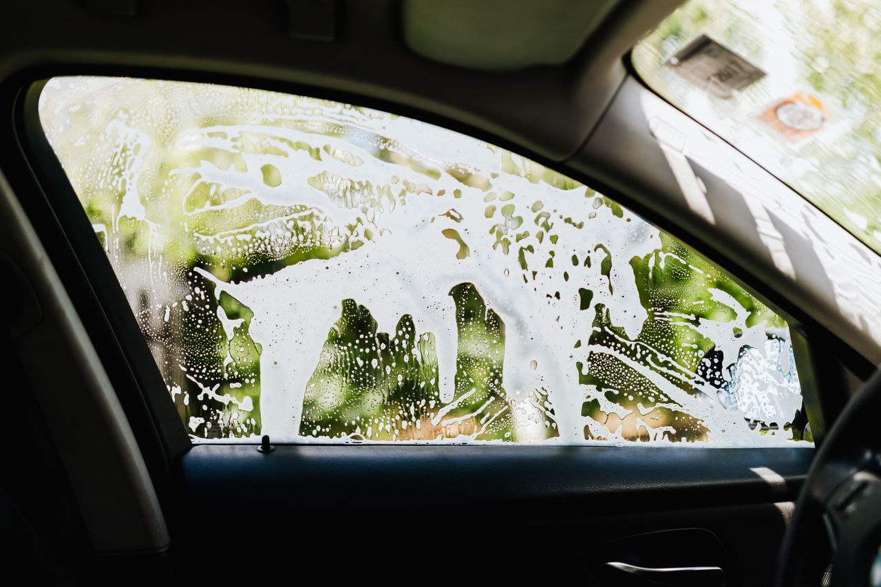 View from inside a car showing soapy water on the window during a car wash.